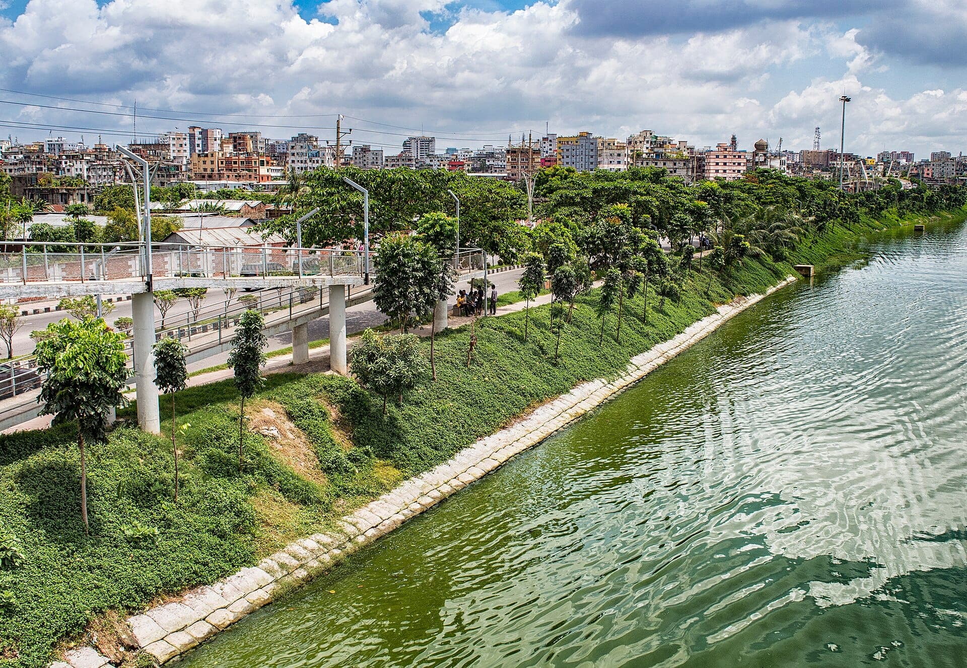 Tree-lined embankment and green water of Hatirjheel lake with the city skyline behind
